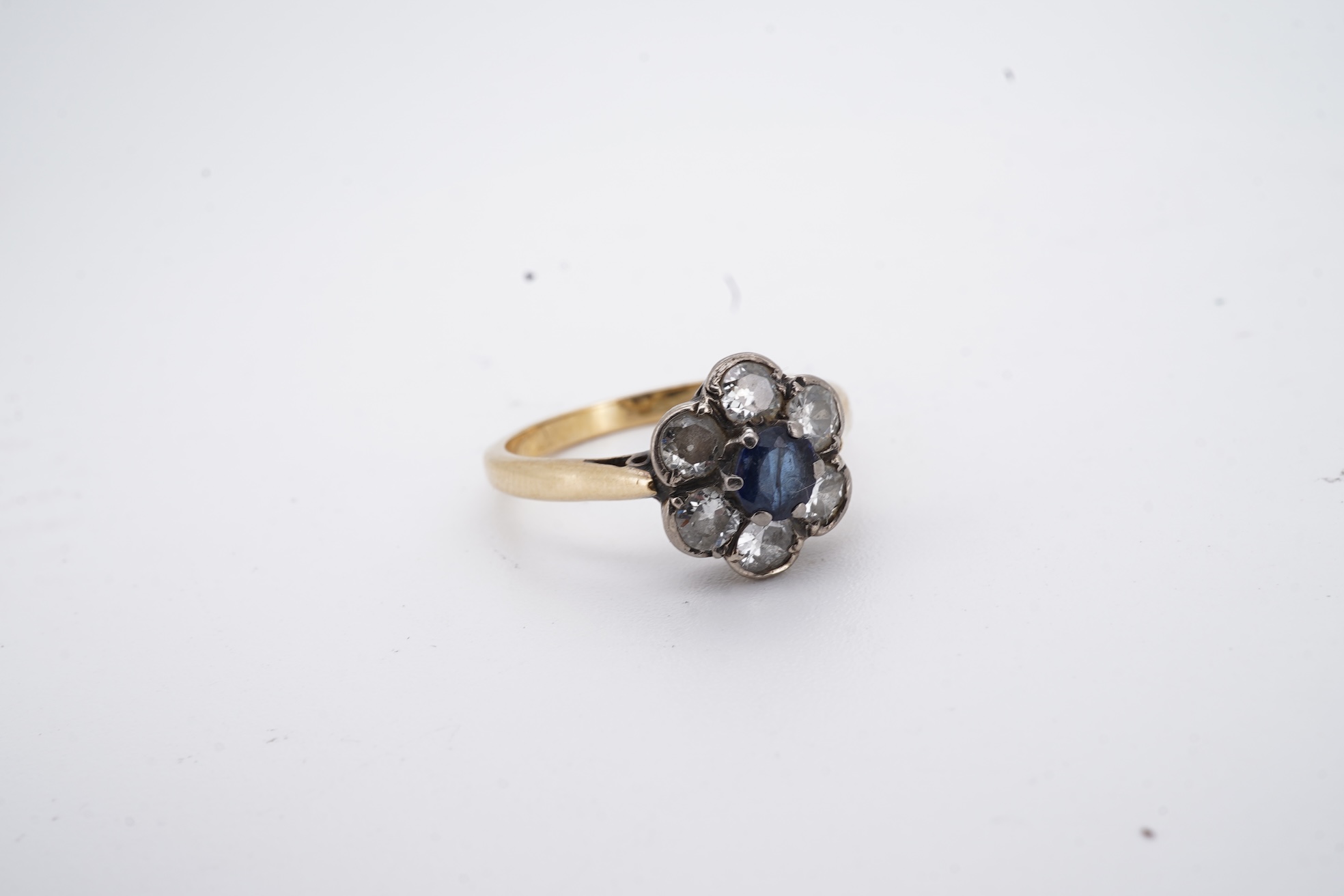 An early to mid 20th century yellow metal (stamped 18ct), singe stone sapphire and six stone diamond set circular cluster ring, size O, gross weight 3.7 grams.